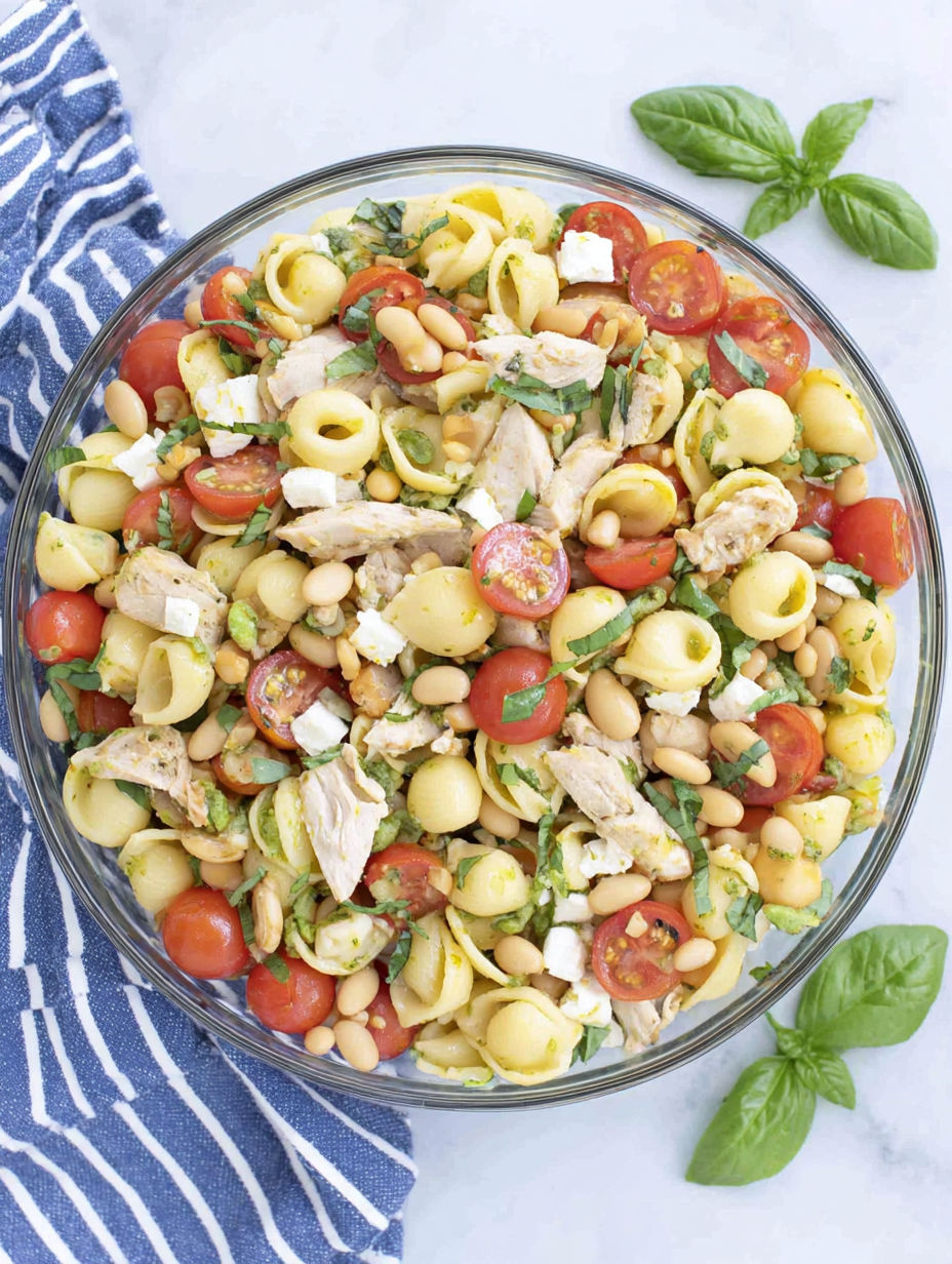 A bowl of pasta salad with chicken, tomatoes, and beans.