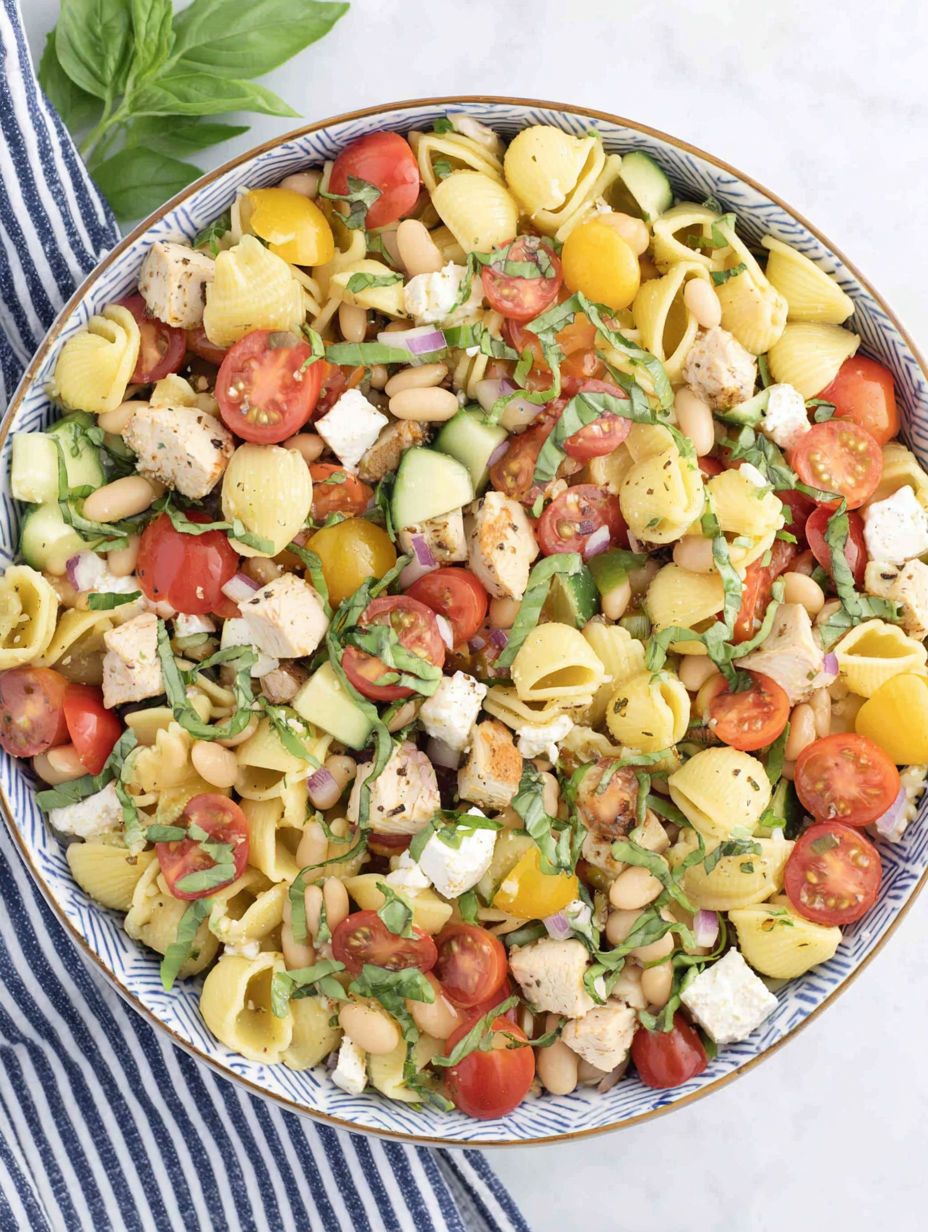 A bowl of pasta salad with chicken, tomatoes, and beans.