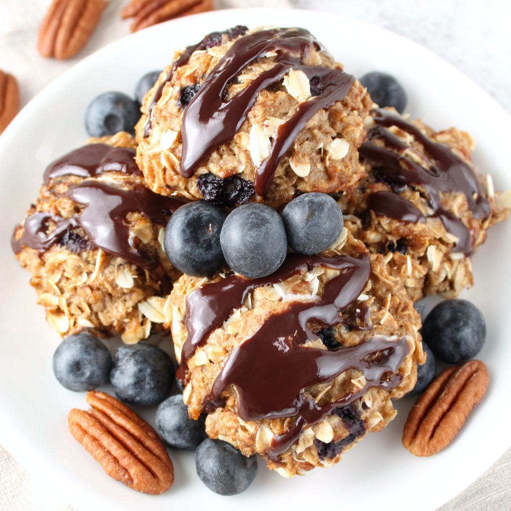 A plate of oatmeal cookies with chocolate drizzle and blueberries.
