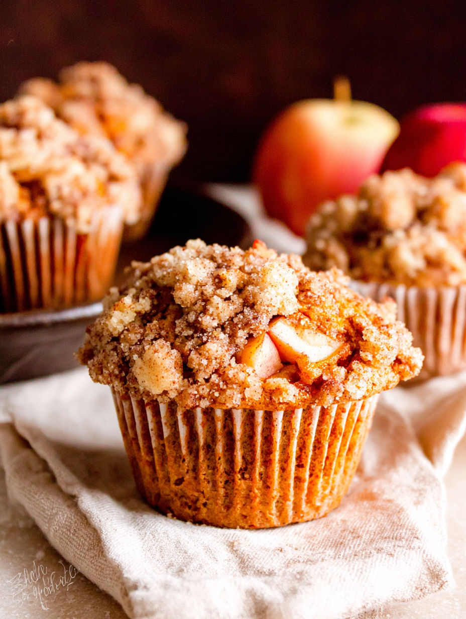 Two muffins with a streusel topping and an apple on the side.