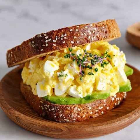 A sandwich with egg salad and cottage cheese on a wooden board.