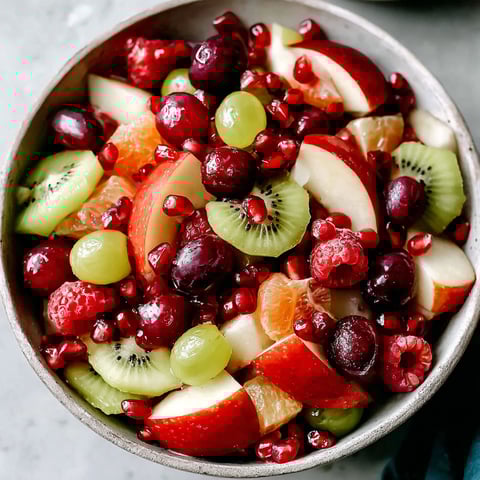 A bowl of fruit salad with kiwi, apples, oranges, and pomegranates.