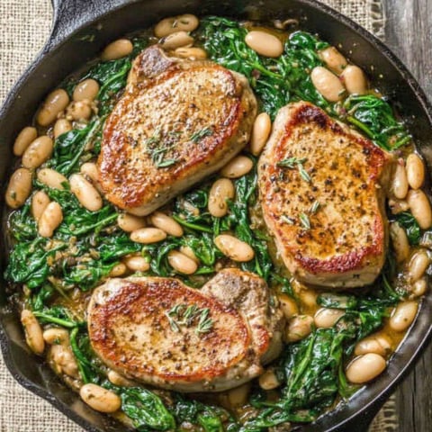 A skillet dinner with pork chops, white beans, and spinach.