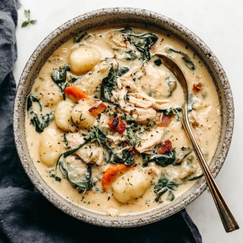 A bowl of soup with chicken, gnocchi, and greens.
