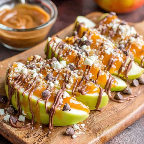 Caramel apple slices on a wooden cutting board.