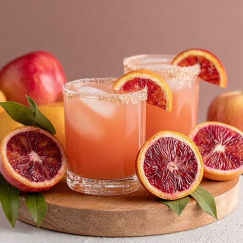 Two glasses of blood orange margarita with slices of blood orange in the background.
