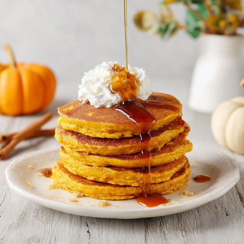 A stack of fluffy pumpkin pancakes with syrup drizzled on top.