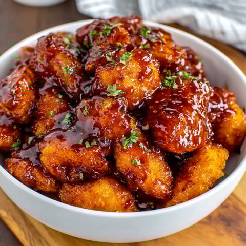 A bowl of orange chicken with sauce.